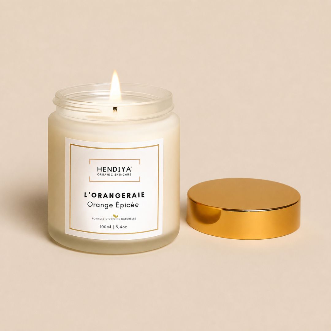 Bougie Végétale l'Orangeraie Hendiya en cire de soja végétale allumée, couvercle doré posé à côté sur fond beige, senteur orange épicée aux écorces de cannelier.