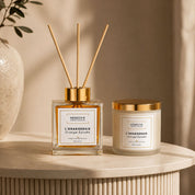 Duo senteur orange épicée Hendiya : flacon diffuseur Parfum d'Ambiance l'Orangeraie 100ml avec tiges de rotin et Bougie Végétale l'Orangeraie en cire de soja naturelle, posés ensemble sur une table ronde.